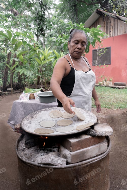 Preview: A senior Hispanic woman is cooking traditional corn tortillas over an outdoor stove