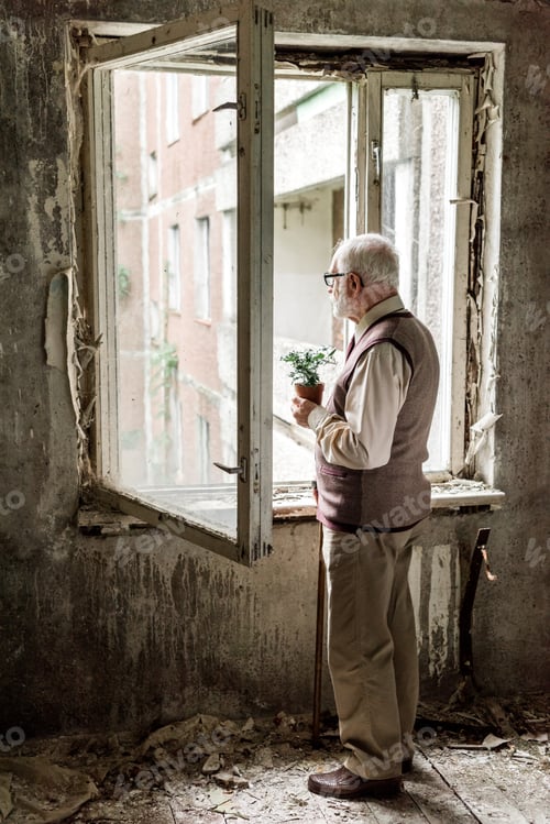 Preview: retired bearded man in glasses holding plant near window in room