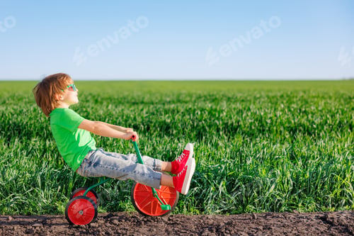 Preview: Happy child riding bike outdoor in spring green field