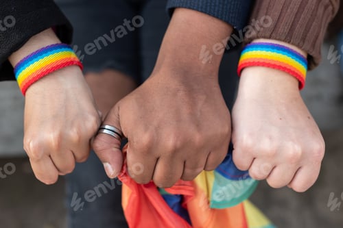 Preview: Close up of three hands with LGBTQ rainbow wristband and holding a Rainbow flag,