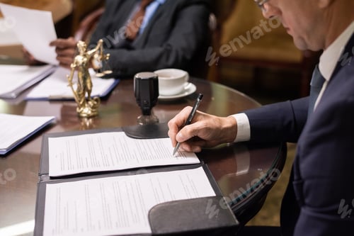 Preview: Mature businessman or jurist signing document by workplace