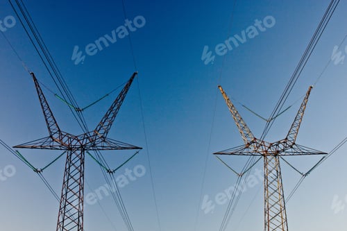 Preview: Low angle shot of two electric towers with a blue sky in the background