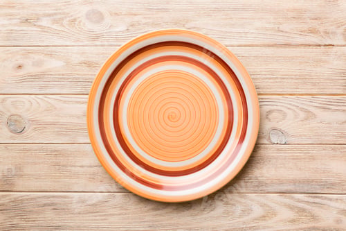 Preview: Top view of empty orange plate on wooden background. Empty space for your design