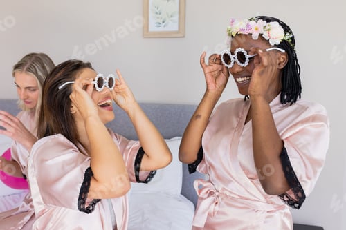 Preview: Women in robes laughing and trying on fun sunglasses during bridal shower