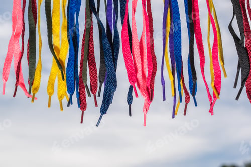 Preview: many colored shoelaces, hanging on a background of sky and clouds, pointed down