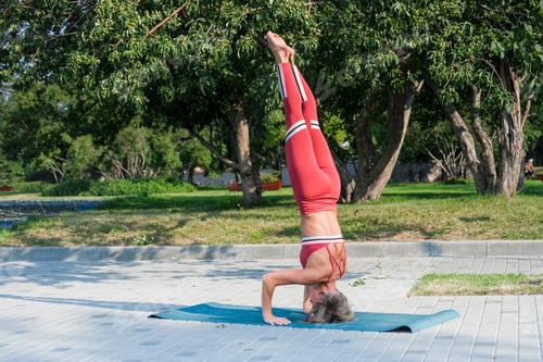 Preview: Woman In Red Sportswear Practices Yoga Exercises In Headstand Posture.