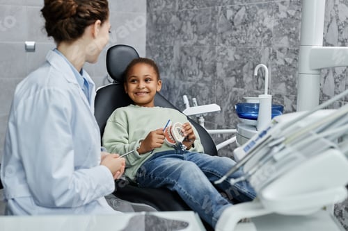 Preview: Smiling little girl sitting in dental chair and listening to female dentist