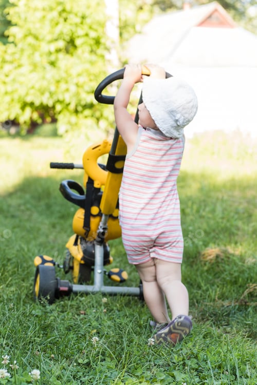 Preview: A little girl is carrying her tricycle, holding on to her parent's handle. International Bicycle Day
