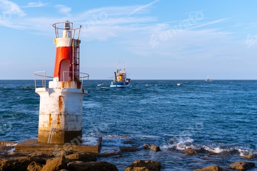 Lighthouse on Rocky Shore with Fishing Boat in Distance