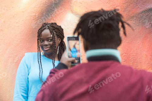 Preview: Black guy taking a photo with his mobile of his girlfriend.