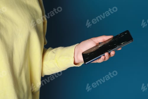 Preview: Woman holding damaged smartphone on light blue background, closeup. Device repairing