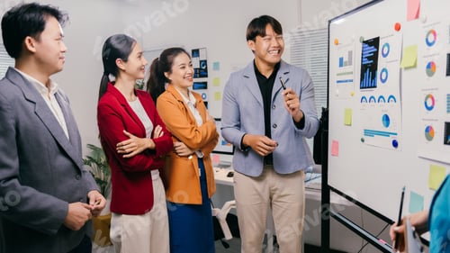 Preview: Young businesspeople smiling and discussing marketing data on whiteboard during a presentation in a
