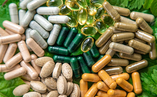 Preview: Capsules herb supplements on green leaves background. Selective focus.