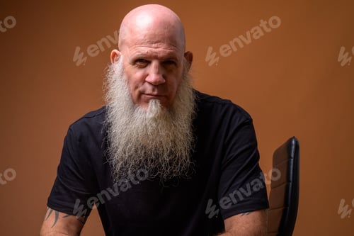 Preview: Mature bald man with long gray beard against brown background