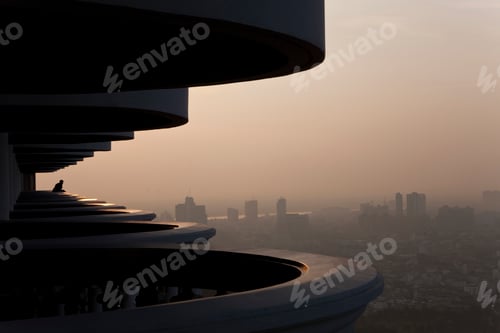 Preview: Man standing on curved balcony on skyscraper, looking over misty cityscape.