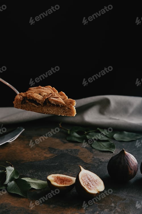 Preview: close up view of piece of pie on cake server and figs on dark grungy surface with black background