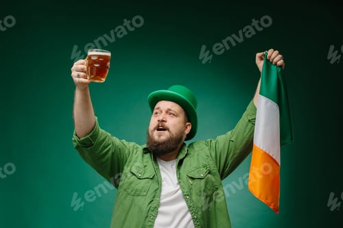 Preview: Happy bearded man with glass of beer and Irish flag on dark green background. St. Patrick's Day.