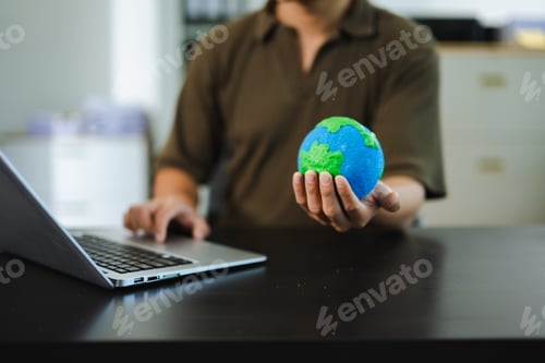 Preview: Young man holding earth model and phone in office, symbolizing green tech, global connection,