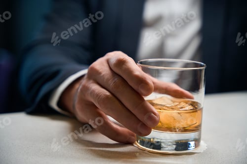 Preview: Close up of glass cup with cognac or whiskey in hands of blurred businessman