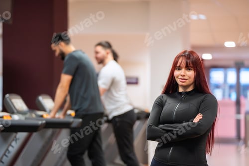 Preview: Confident woman in front of gym equipment, smiling softly.