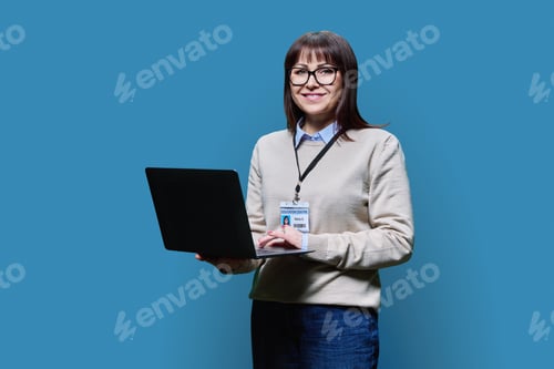 Preview: Middle aged confident serious female teacher using laptop on blue background