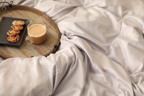 Preview: Delicious cookies and cup of coffee on bed with stylish silky linens, space for text