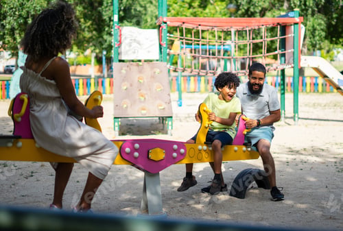 Preview: Latin family with their 8-year-old son playing together on a swing at a playground