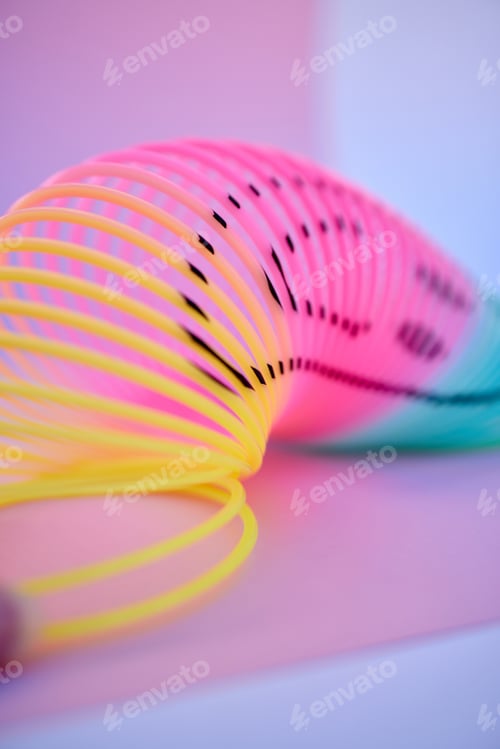 Preview: A brightly coloured neon slinky isolated against a multicoloured background in studio. A fun and im
