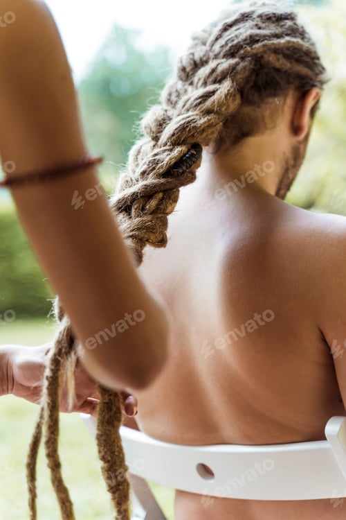 Preview: Close-up of a girl's hands, braiding a boy's dreadlocks in the garden.
