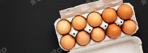 Preview: Raw Brown Eggs in a paper box on a black background, top view. Flat lay, overhead