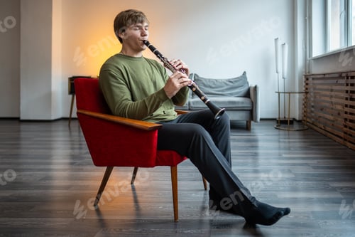 Preview: Clarinet player. Man clarinetist playing flute woodwind music instrument sitting on armchair at home
