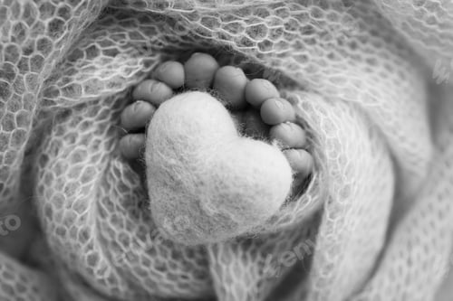 Preview: Knitted heart in the legs of baby. The tiny foot of a newborn baby.