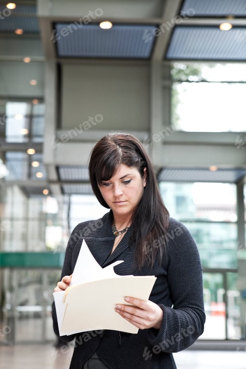 Preview: A young caucasian businesswoman going through paperwork in a convention center lobby area.