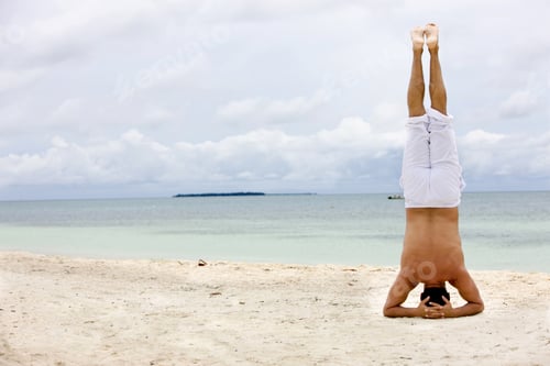 Preview: Handsome Man Upside-Down Meditating At The Beach