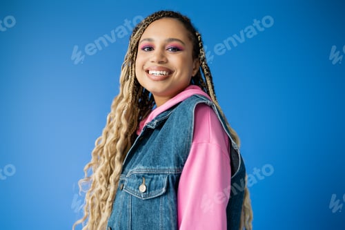 Preview: beautiful african american woman in pink hoodie and denim vest on blue background, dark skinned