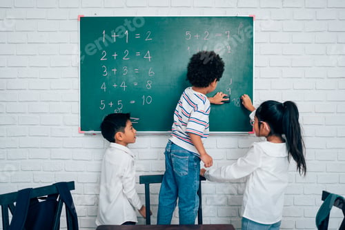 Preview: little child standing at chalkboard and writing math formula on blackboard.