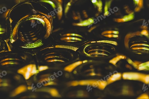 Preview: Closeup shot of small metal screw nuts in a dark atmosphere with yellow lights on them