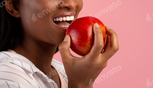 Preview: Dental care. Cropped view of black lady with healthy teeth eating ripe red apple over pink