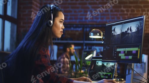 Preview: Side View Of Casual Korean Girl Wearing Headphones And Editing Video In Office Working At Table