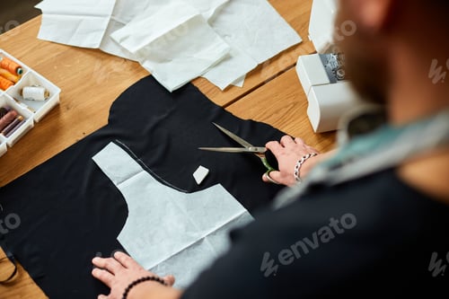 Preview: Man dressmaker cutting material with scissors on table, male tailor working in atelier