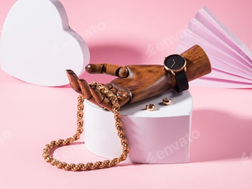 Preview: Fashion scene with golden accessories in wooden hand on white heart shape podium