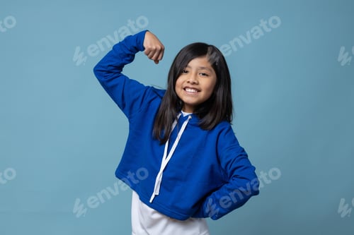Preview: Happy Mexican girl showing arm muscle and having fun over blue background