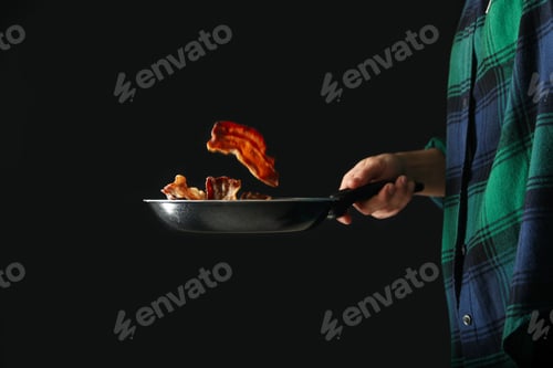 Preview: Woman fries bacon in a frying pan on a black background