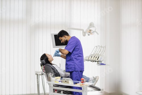 Preview: Bearded male dentist treating teeth of a young asian woman using tooth drill