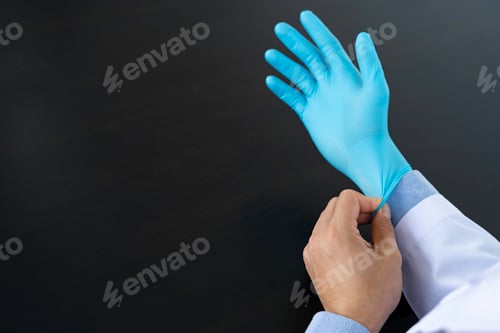Preview: Putting on a Protective Blue Glove Over Black Background