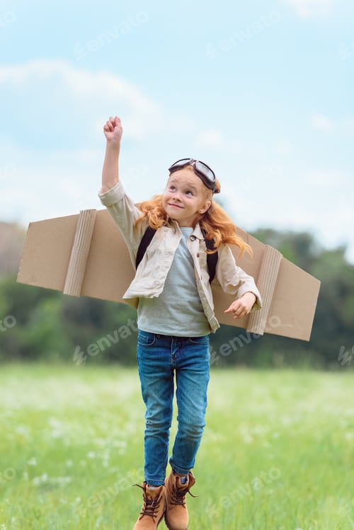 Preview: kid in pilot costume with outstretched arm jumping in meadow