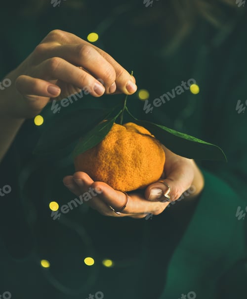 Preview: Fresh tangerine fruit in hands of lady wearing green dress