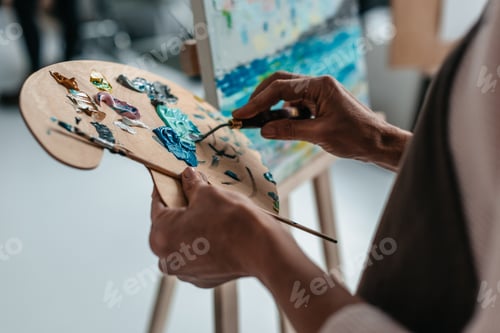 Preview: cropped shot of artist holding palette and paintbrush in art studio