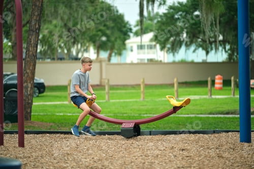 Preview: Young handsome teenage boy playing alone on swings on summer vacations sunny day
