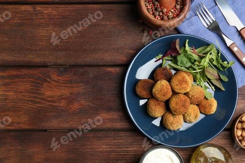 Preview: Delicious falafel balls with herbs served on wooden table, flat lay. Space for text